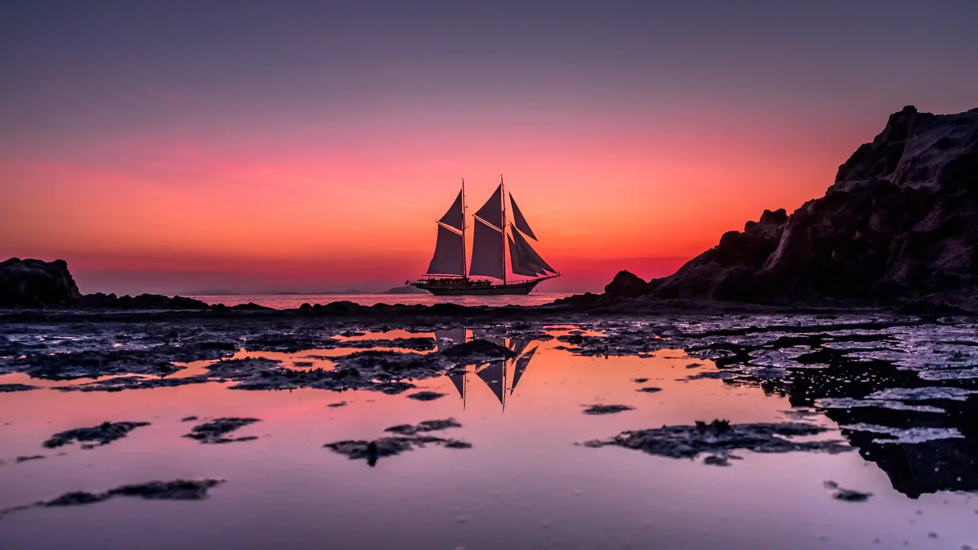 A traditional phinisi silhouetted against a Komodo sunset